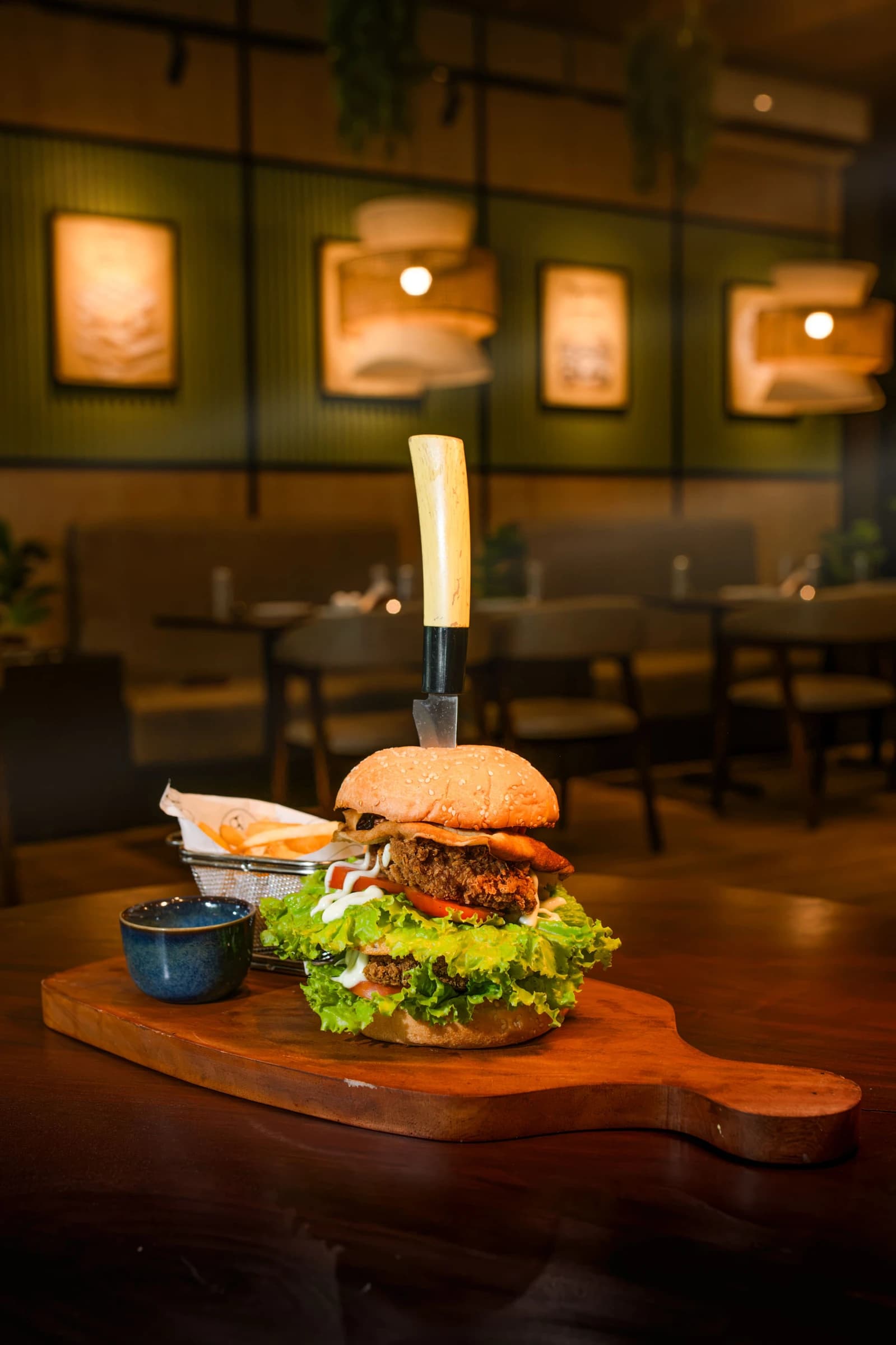 Burger and fries on a wooden serving board in a warmly lit restaurant