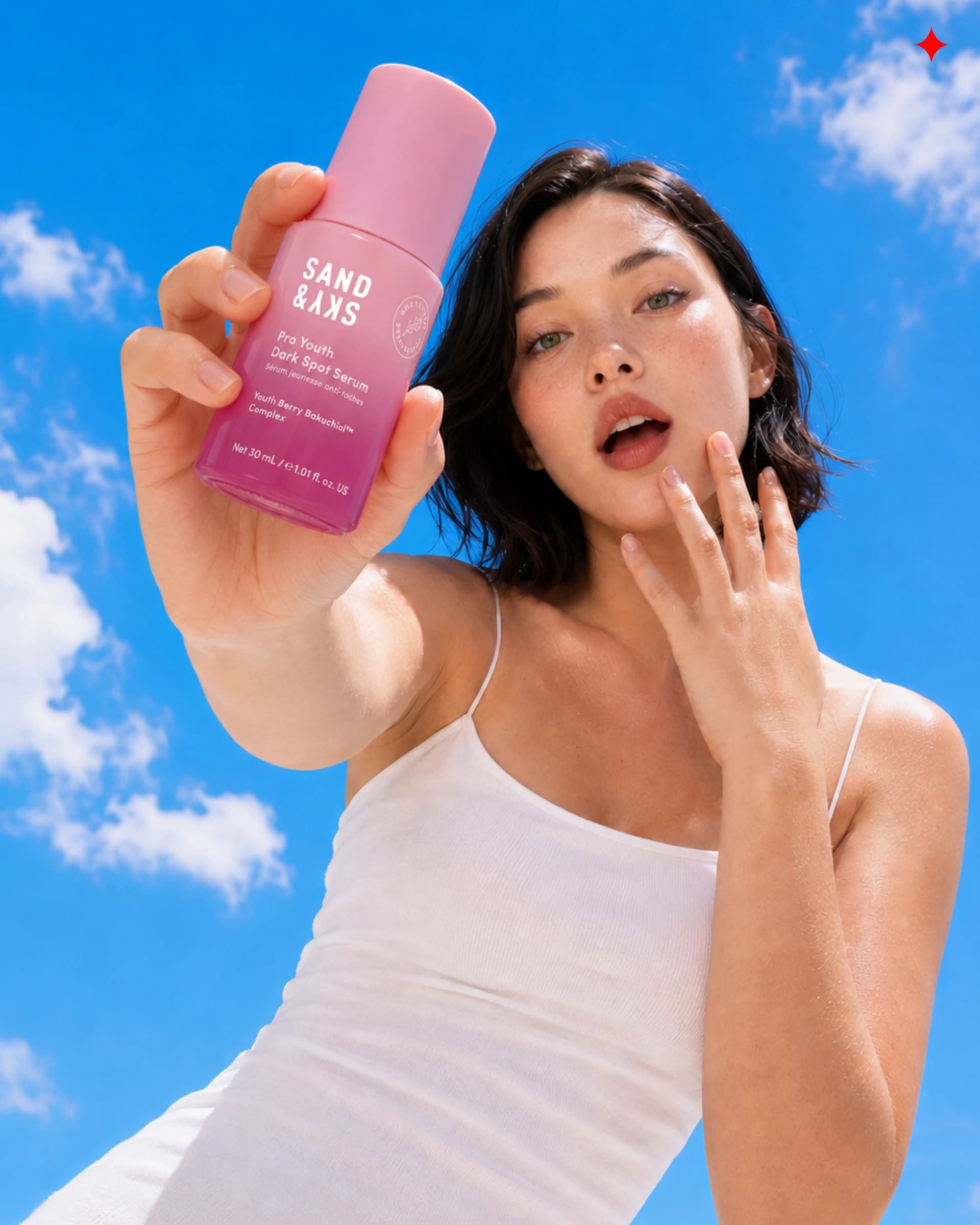 Woman holding a pink Sand & Sky skincare bottle against a blue sky